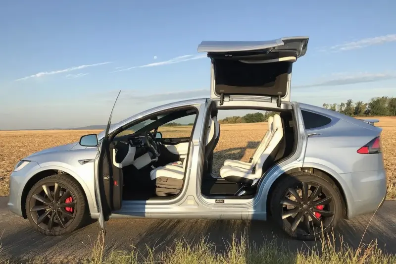 Tesla Model X plata de lado, con las puertas de ala de halcón abiertas y los asientos blancos a la vista