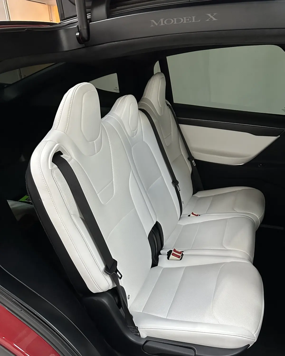 Asientos traseros blancos del Tesla Model X bajo la puerta de ala de halcón abierta